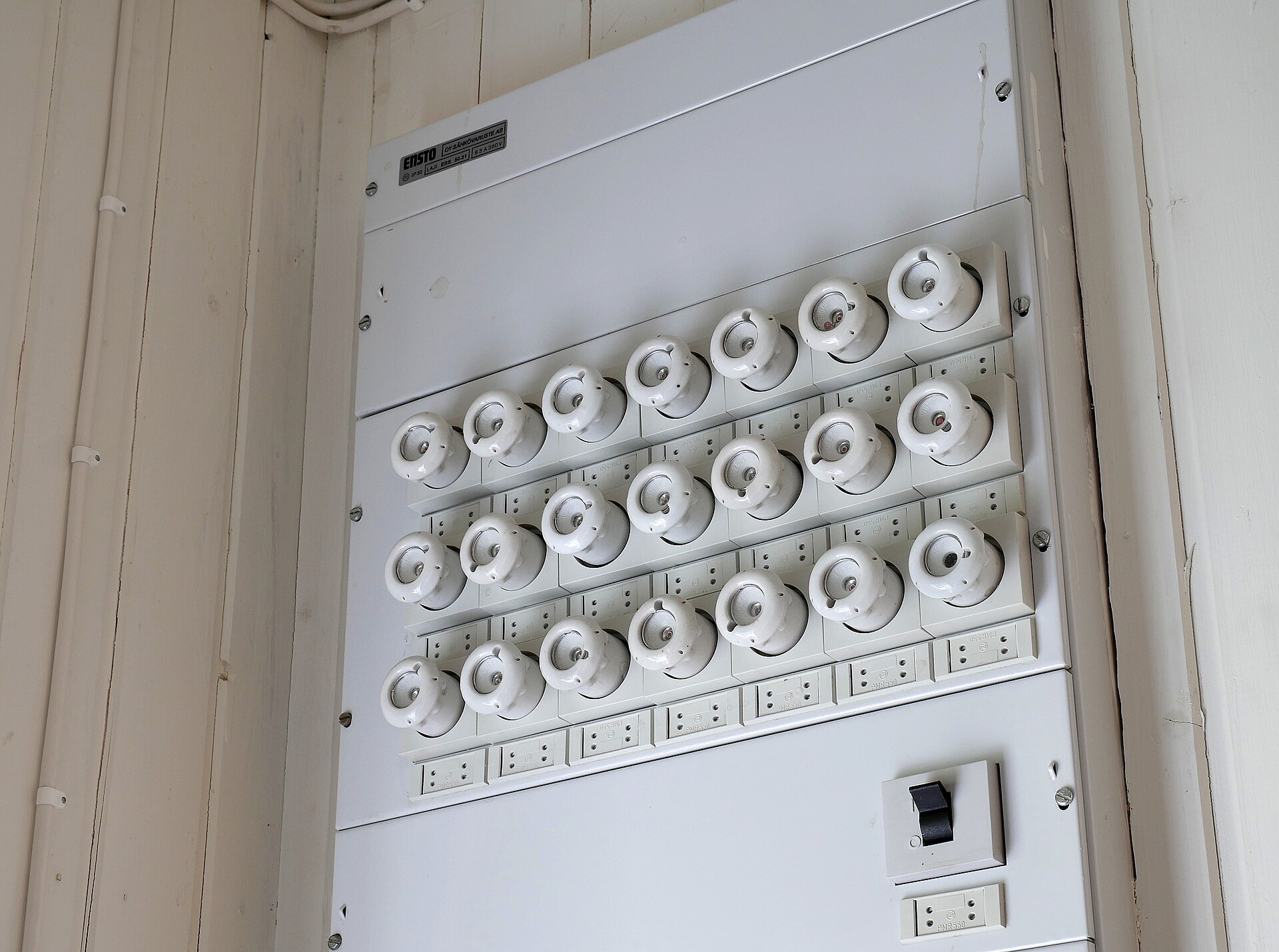 Rows of white ceramic screw-in fuses on an old wall-mounted fuse board, each fuse guarding its own circuit.