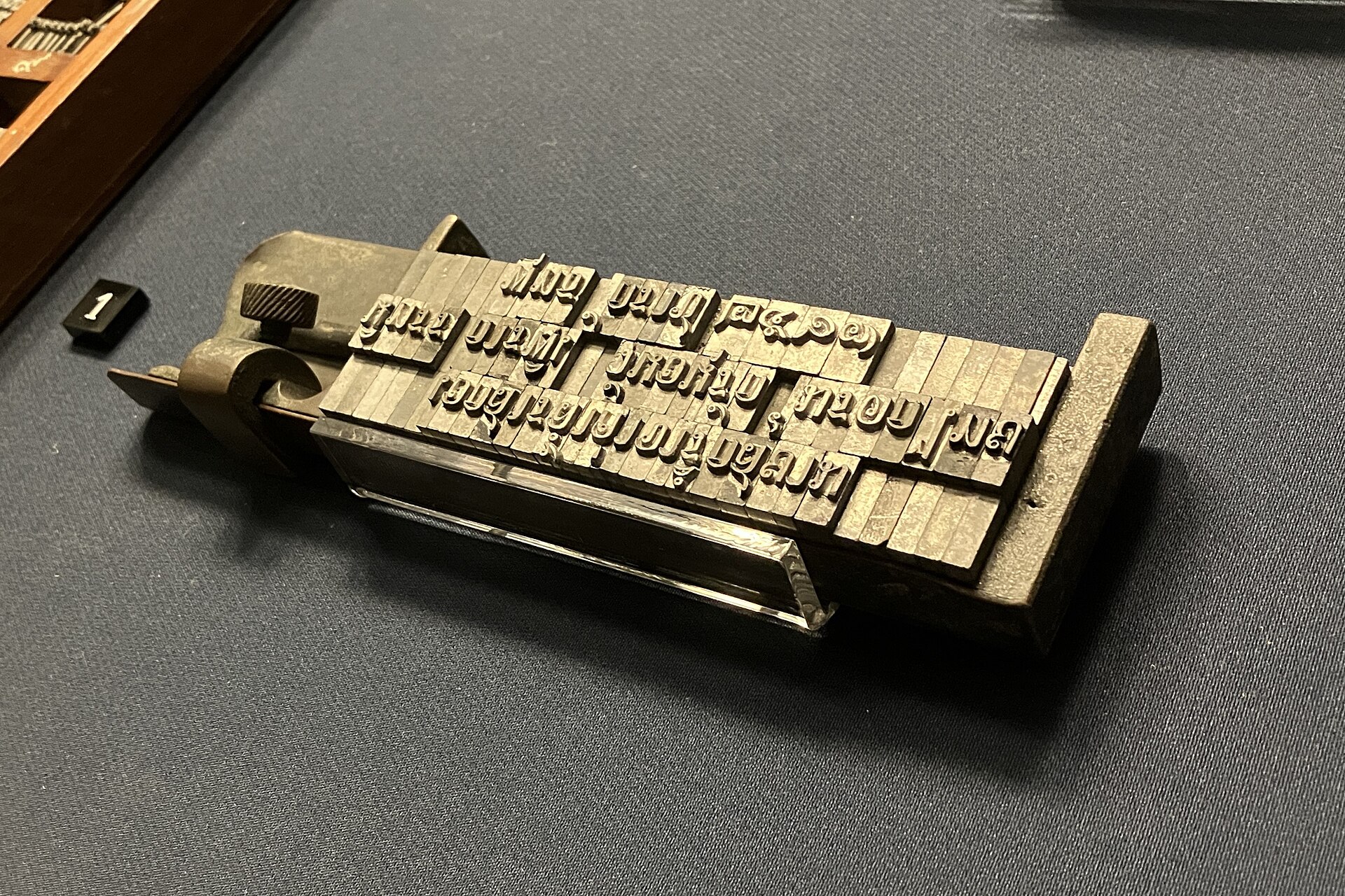 Metal movable type for the Thai script assembled and clamped in a composing stick, resting on dark cloth in a museum display.
