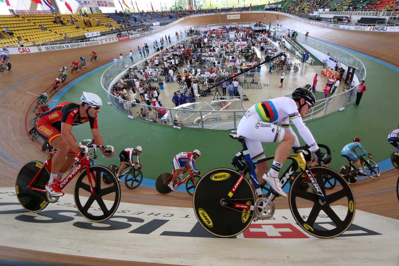 Track cyclists leaning through a banked turn around a crowded velodrome in Cali.