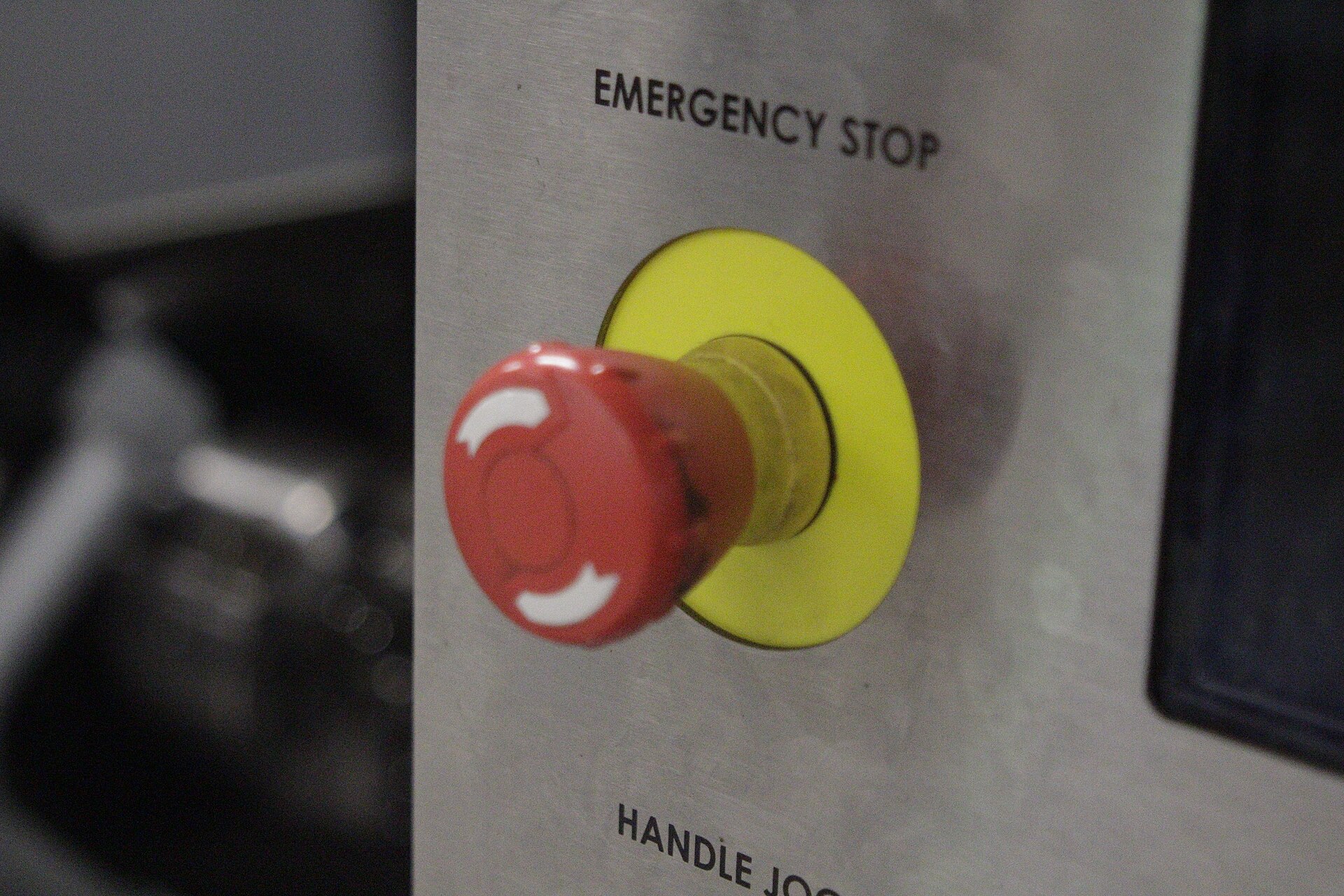 Close-up of a red emergency stop button on a yellow ring, mounted on the metal control panel of a CNC machine.