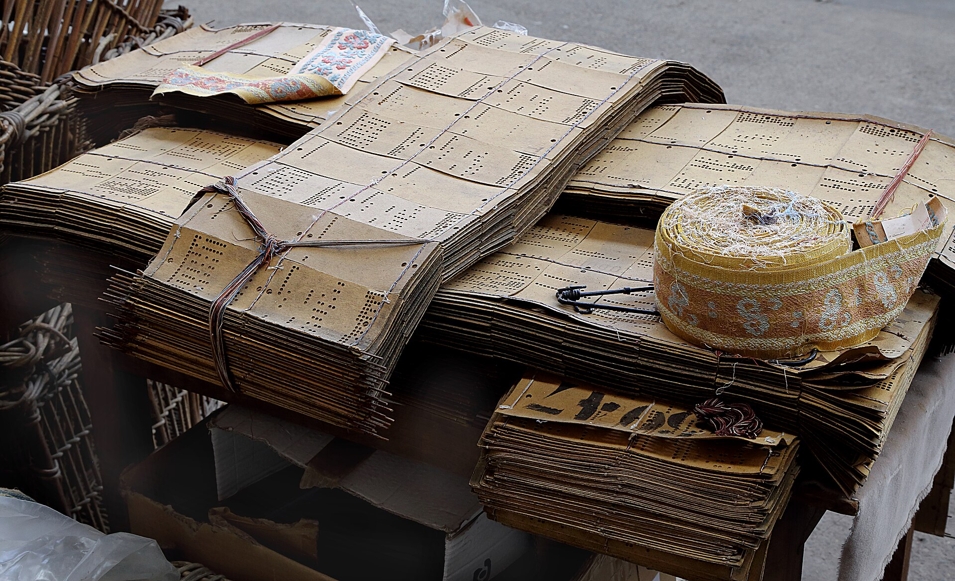 Stacks of linked weaving punch cards with a roll of patterned ribbon.