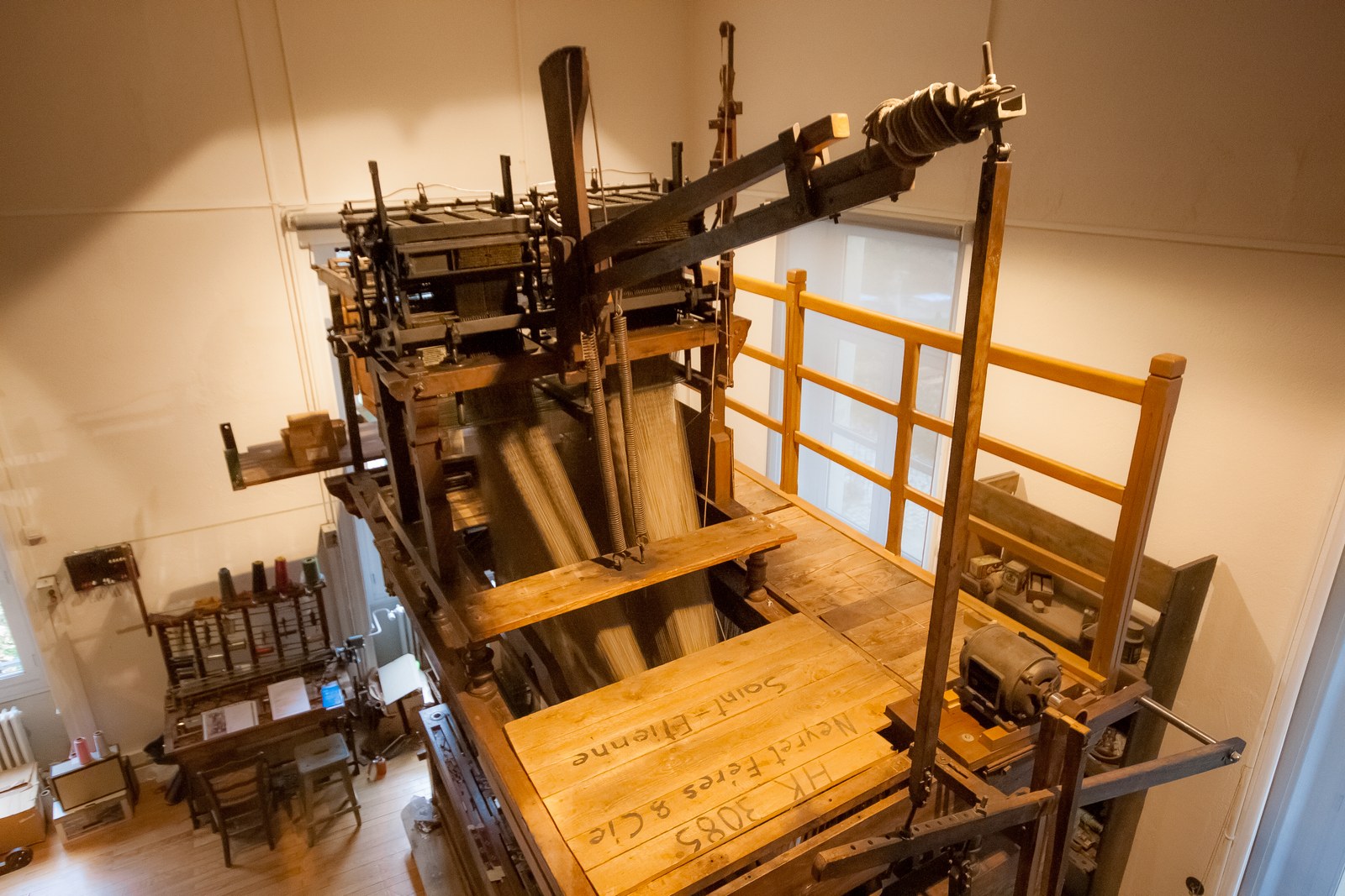 A large wooden Jacquard loom seen from above, with threads and lifting mechanisms exposed inside a museum.
