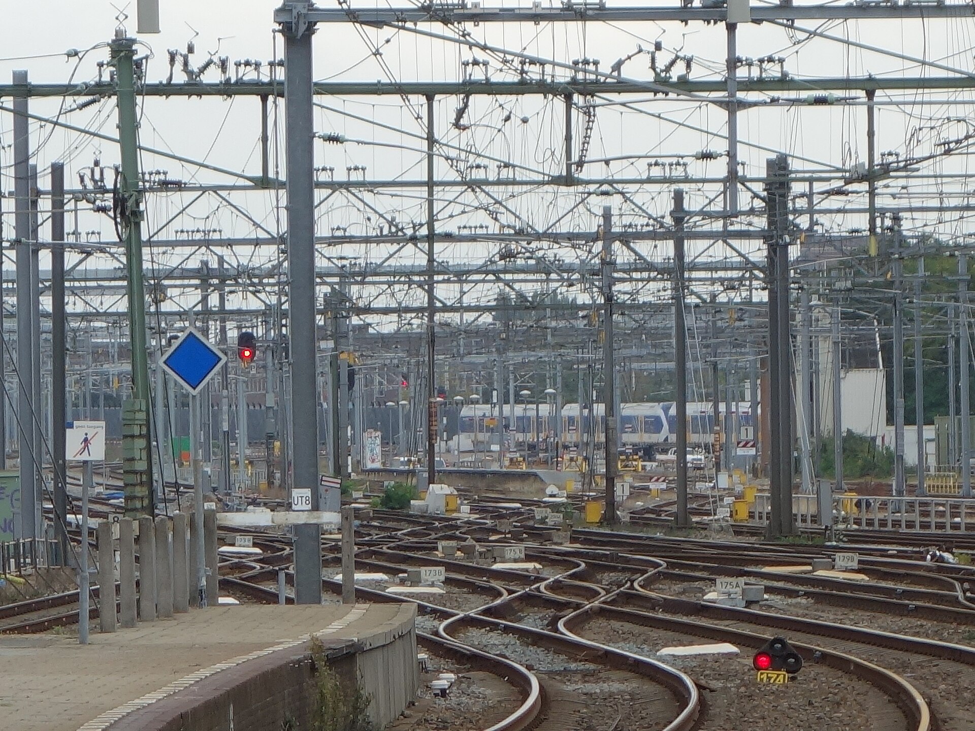 A dense field of railway switches and crisscrossing tracks in front of Utrecht Centraal station, under a web of overhead wires.