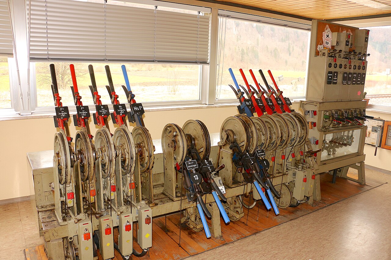 A mechanical railway interlocking frame with red, blue, and black levers lined up beside a control panel.
